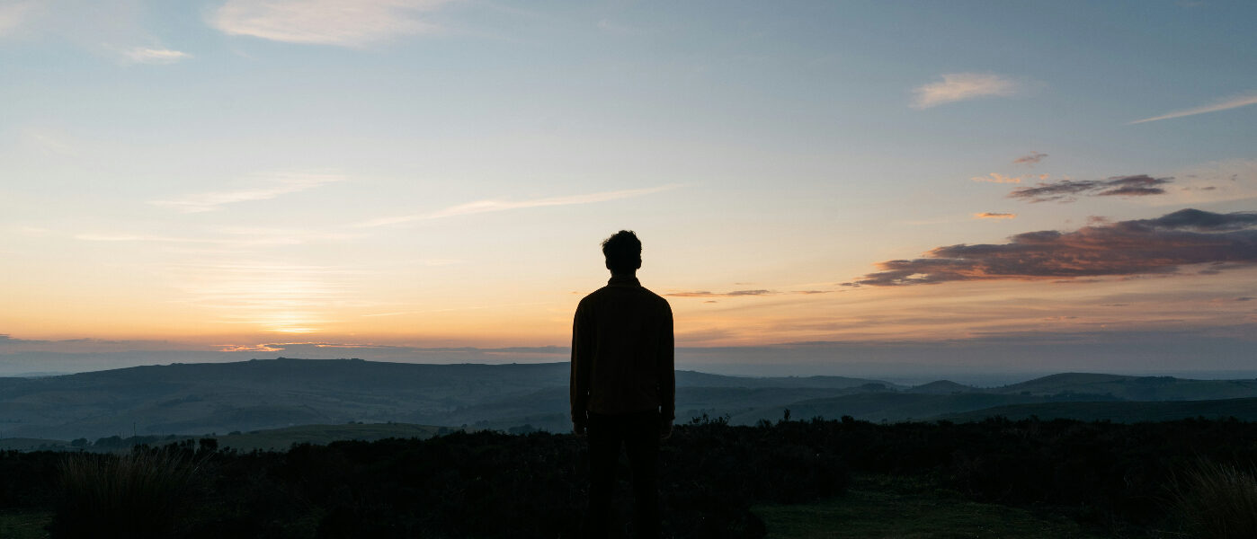 “A Question to Sit With” photo with man looking towards the end of a sunset over the mountains.